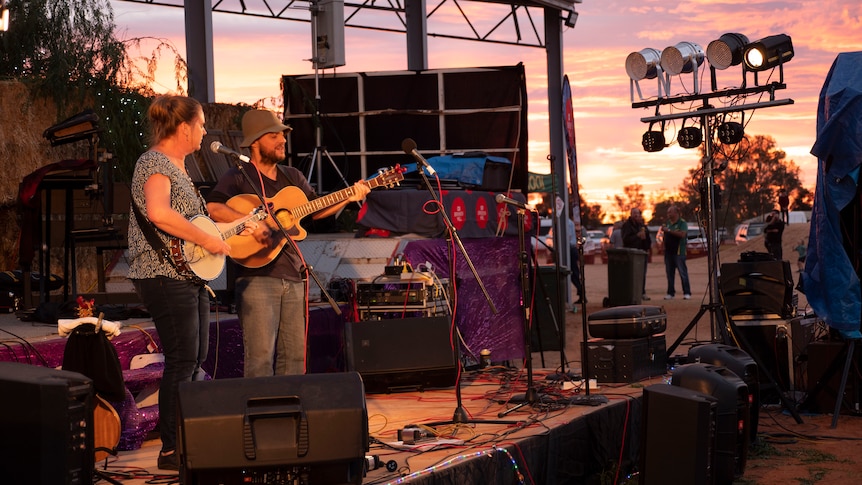 A man and a woman play and sing on an outdoor stage.