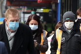 Pedestrians walk along a Melbourne CBD street, all wearing face masks.