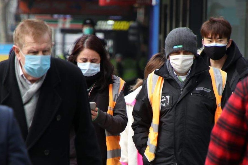 Pedestrians walk along a Melbourne CBD street, all wearing face masks.