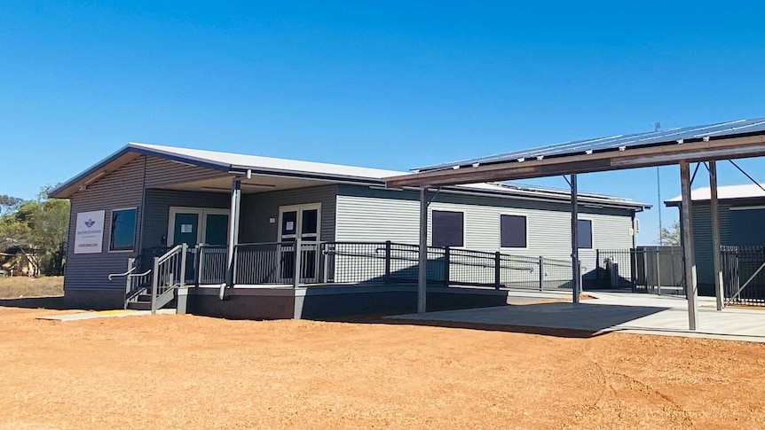 Two modern buildings stand surrounded by outback red dirt. There are steps and ramps leading to the door.