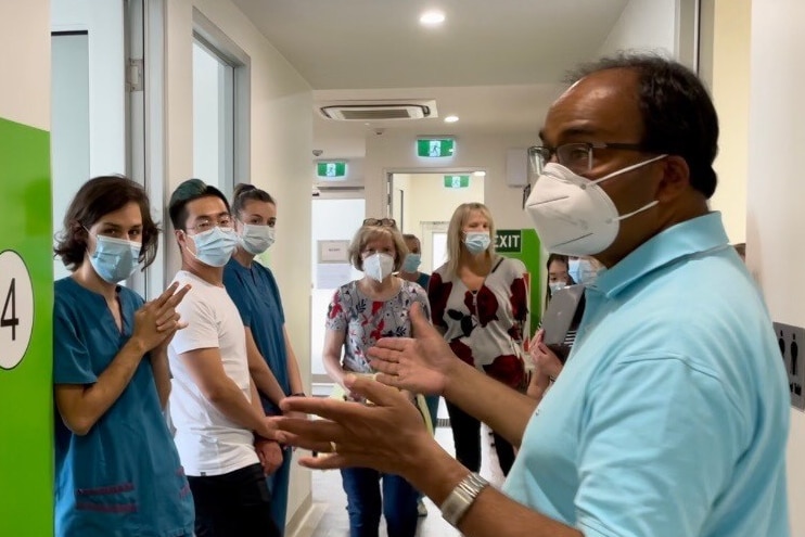 Dr Haikerwal on the far right wearing a blue polo shirt and a mask briefing other medical workers wearing masks
