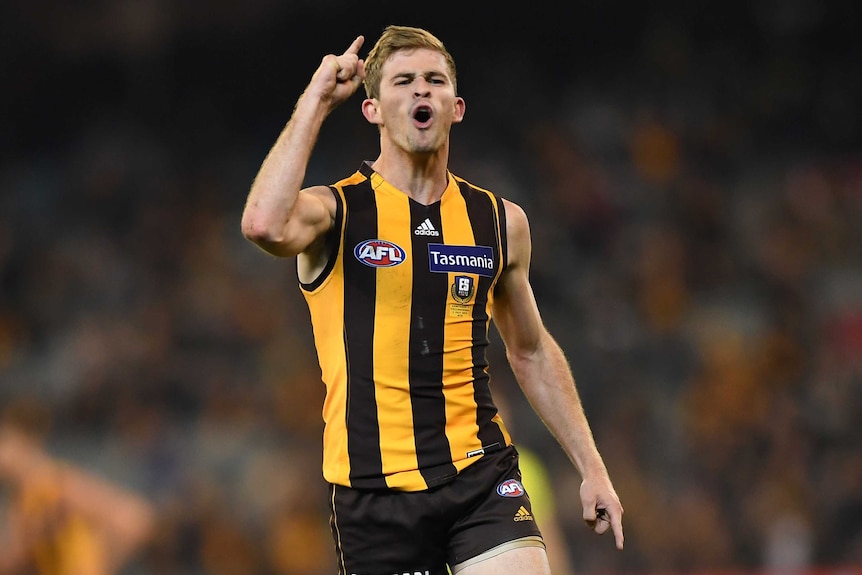 A male AFL player points a finger on his right hand and he screams out to celebrate kicking a goal.