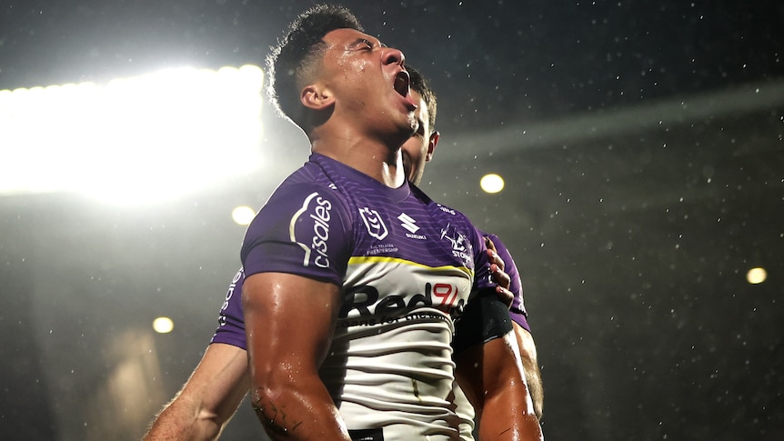 NRL player Dean Ieremia of the Storm celebrates, puffing his chest and screaming, as rain falls