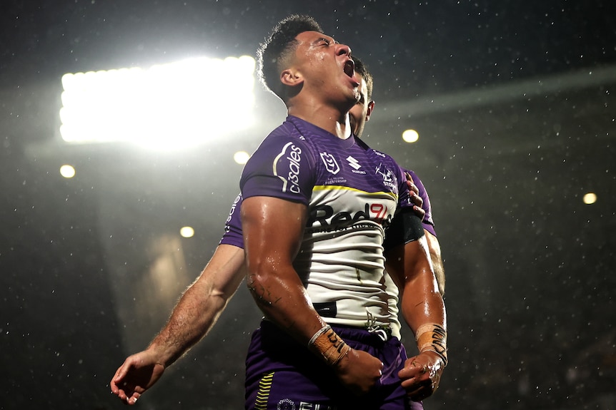NRL player Dean Ieremia of the Storm celebrates, puffing his chest and screaming, as rain falls
