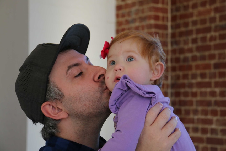 Cameron Pinceus holds up his daughter and kisses her on the cheek.