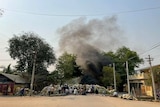 A cloud of smoke hangs above sandbags and people huddled in a rundown Asian village.