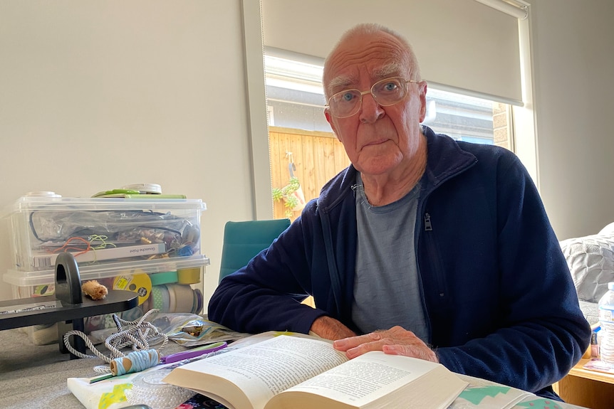 Elderly man looks at camera with a book and his craft in front of him