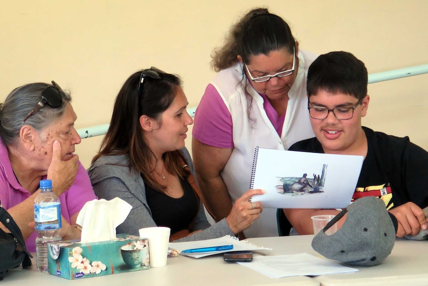 Four people sit at a desk reading a script.