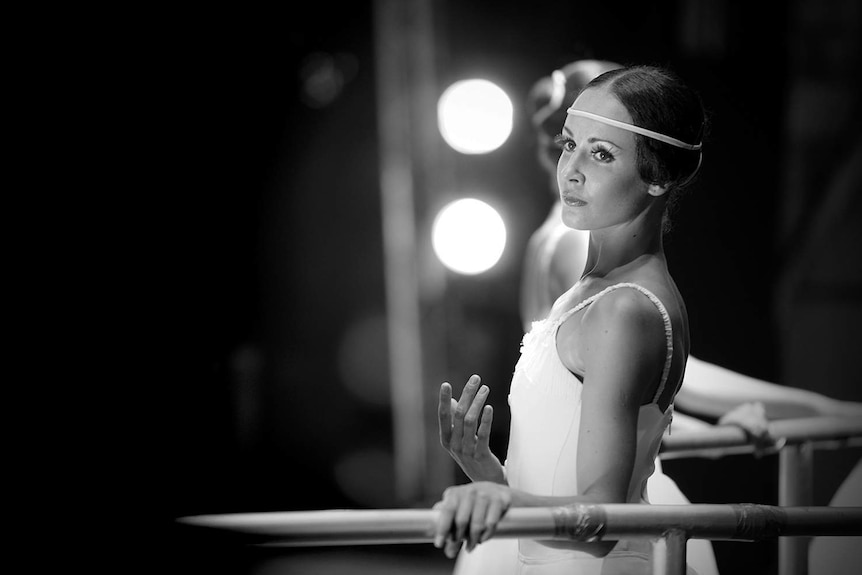 A ballet dancer stands in position at a bar in a tutu