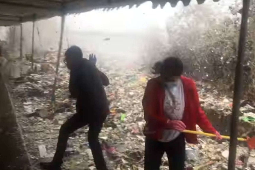 Volunteers jump as the wall of garbage crashes ashore.