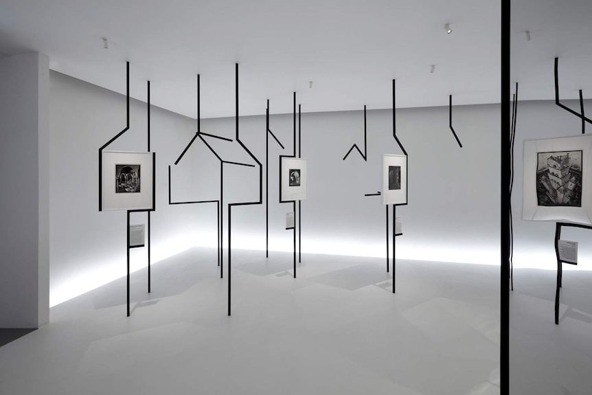 White gallery room with black steel scaffolding with house shapes running floor to ceiling, and Escher works hung throughout.