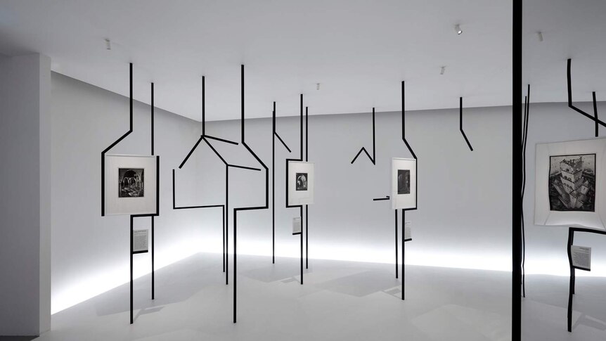 White gallery room with black steel scaffolding with house shapes running floor to ceiling, and Escher works hung throughout.