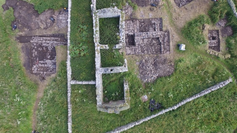 An overhead view of the excavation site shows stone wall and green grass