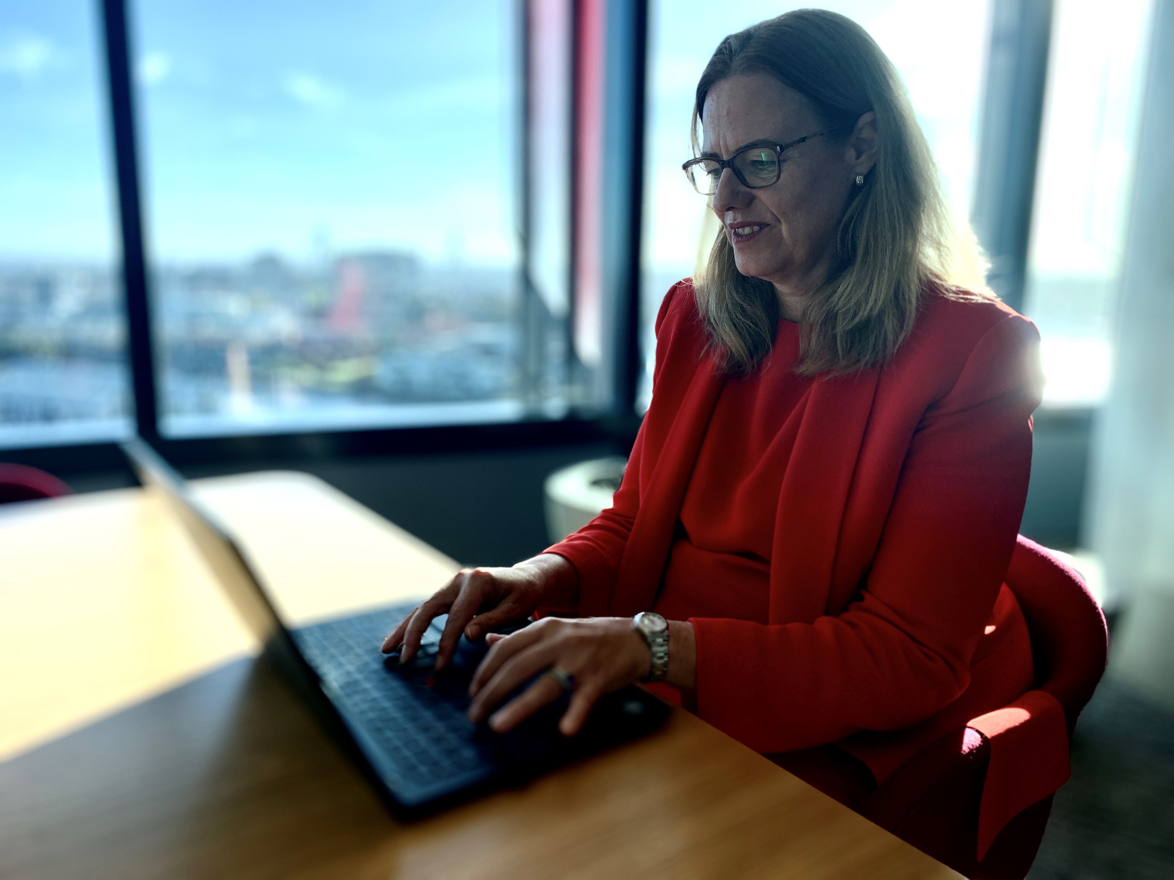 A woman in a red suit types on a laptop