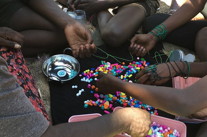 Group of girls sitting around a colourful array of beads making bracelets