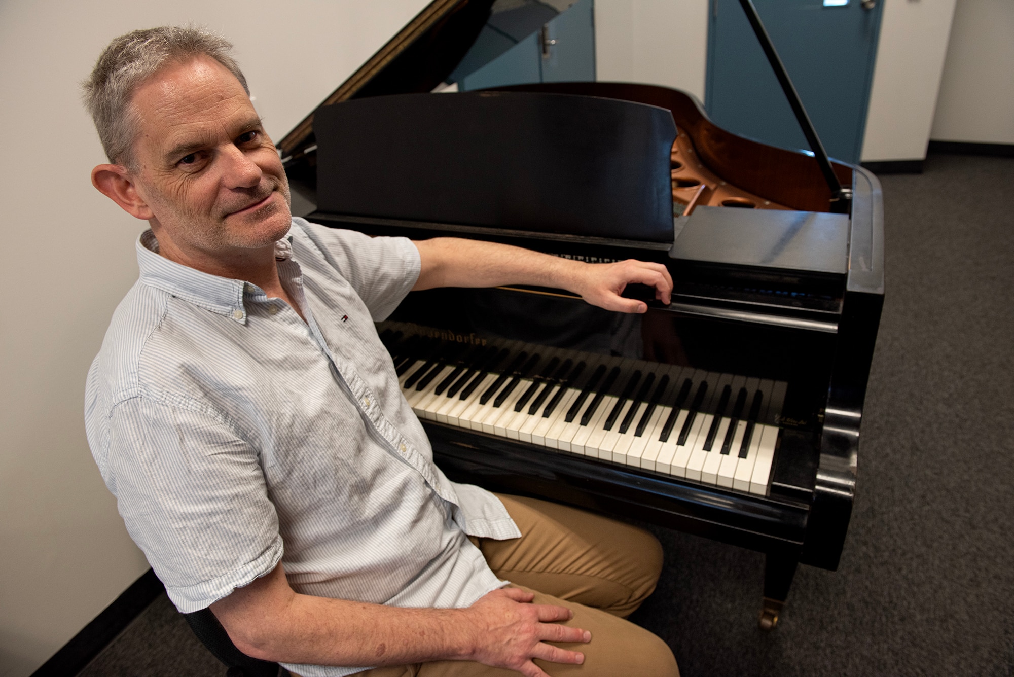 A grey-haired man sits at a piano.