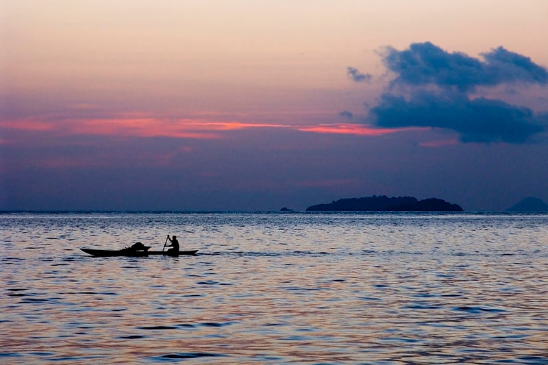 Pink and indigo sky at sunset as person paddles in canoe on ocean north of New Ireland, PNG.