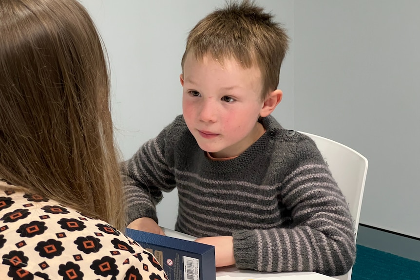 A young boy pays attention to an adult he is facing.