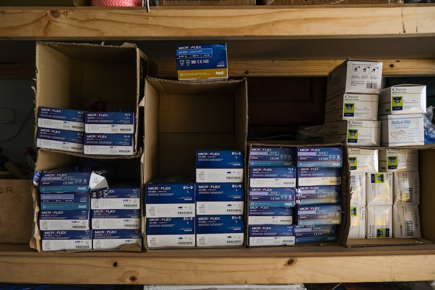 Stacks of boxes of gloves and face masks sitting in a wooden shelf