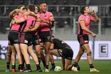 A Penrith NRL player makes a silencing gesture with his finger on his mouth as his teammates celebrate a try in the background.