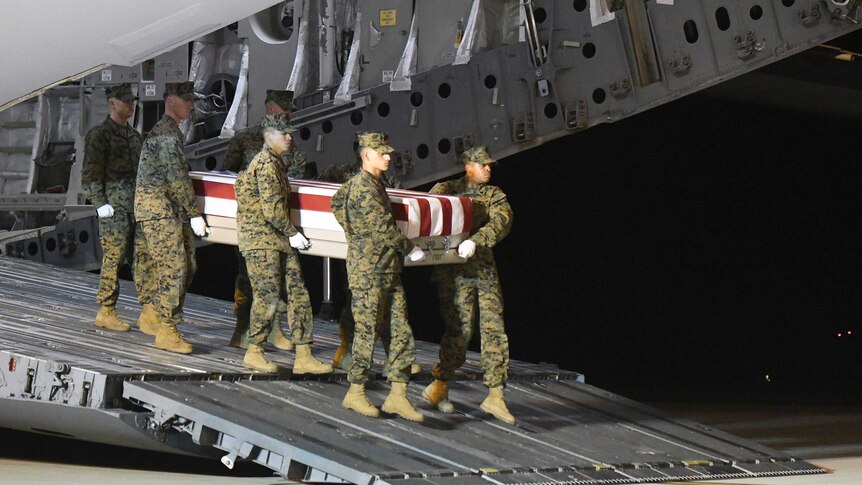 Marines carry a coffin draped in a US flag form the back of a plane.