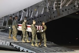 Marines carry a coffin draped in a US flag form the back of a plane.