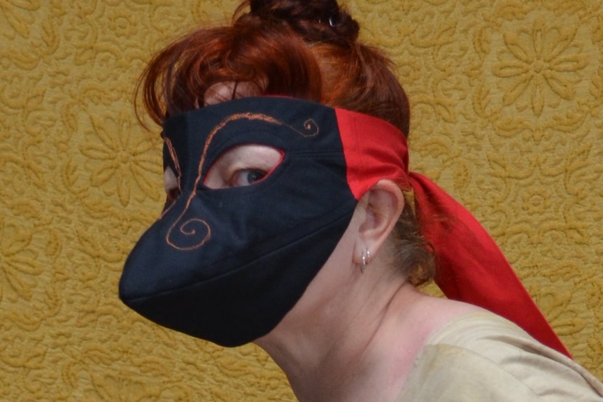 A photo of a woman wearing a black beaked mask covering her whole face, with curled eyebrows stitched above the eye holes.