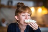 Young woman eating bread with cream cheese.