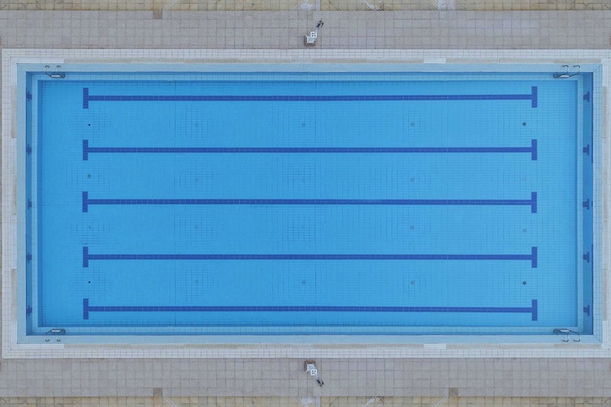 A close-up aerial view of a rectangular swimming pool, with pale tiled edging and bright blue internal tiles.