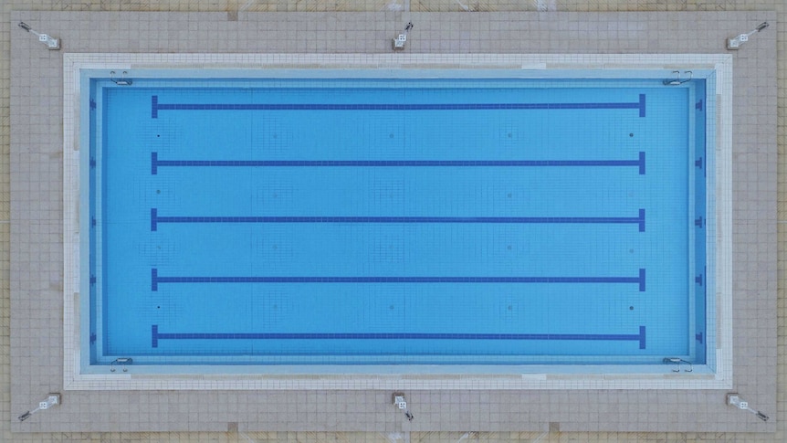 A close-up aerial view of a rectangular swimming pool, with pale tiled edging and bright blue internal tiles.