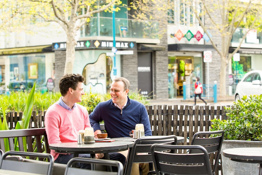 Two men sit together at an outdoor cafe table