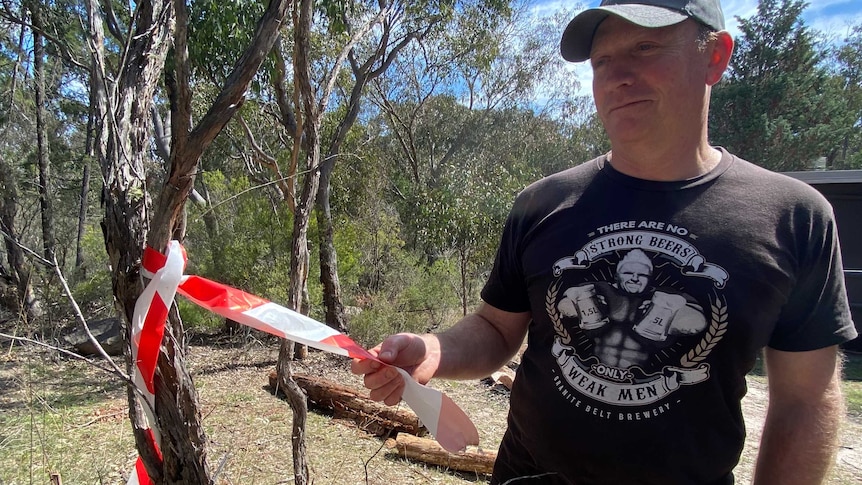 A man stands next to a small tree with red and white fire tape hanging from it