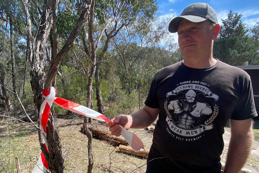 A man stands next to a small tree with red and white fire tape hanging from it