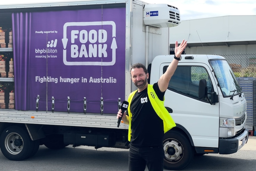 A man in high-vis stands in front of a purple truck with Foodbank WA logo 
