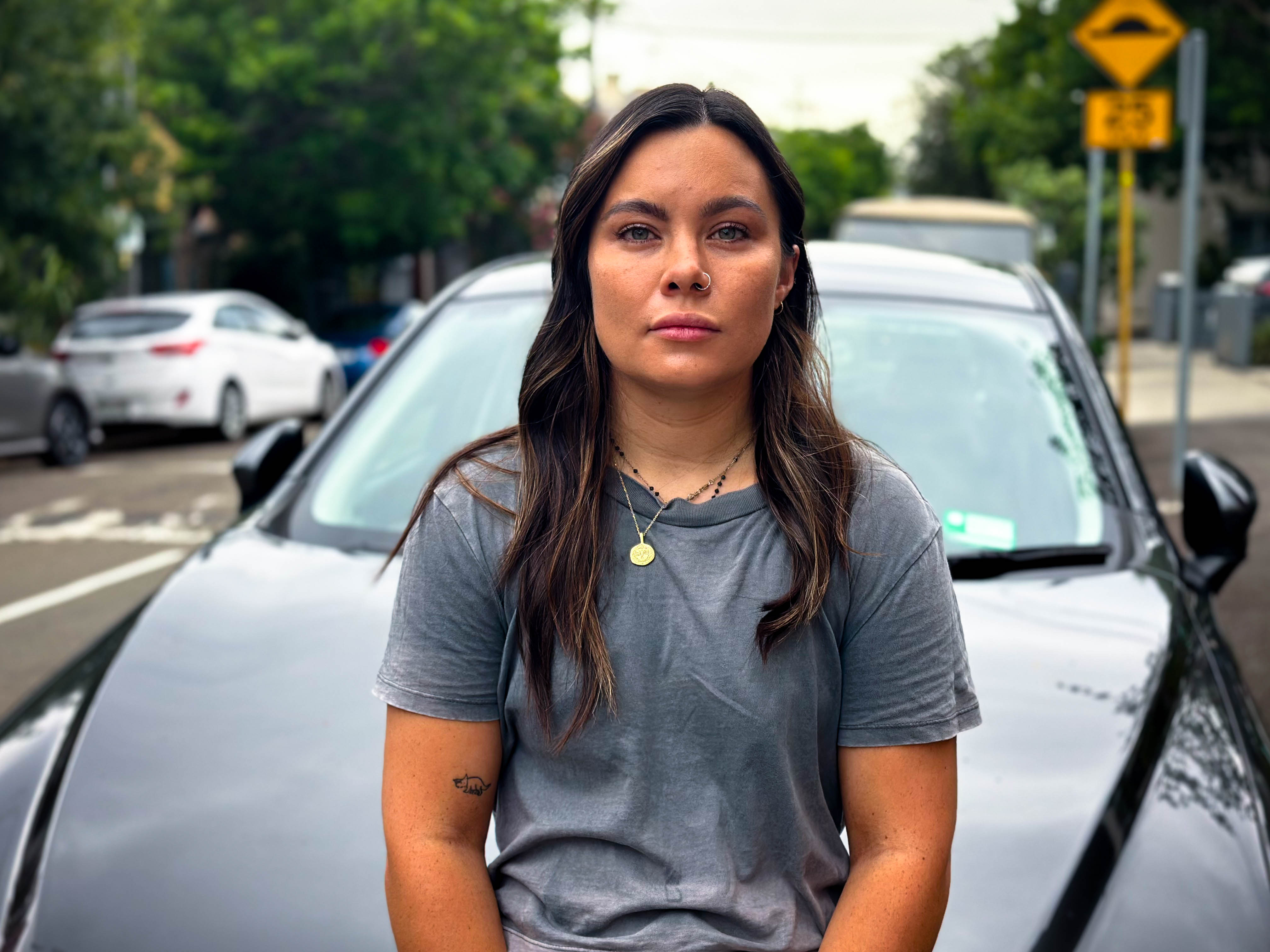 Woman with brown hair sits in front of a car