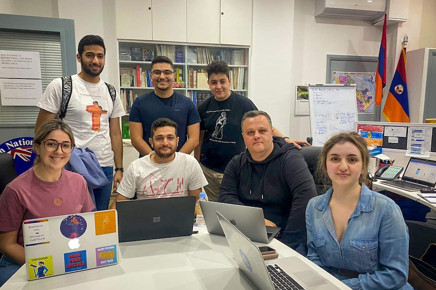 A group of young people sit around a desk with their laptops.