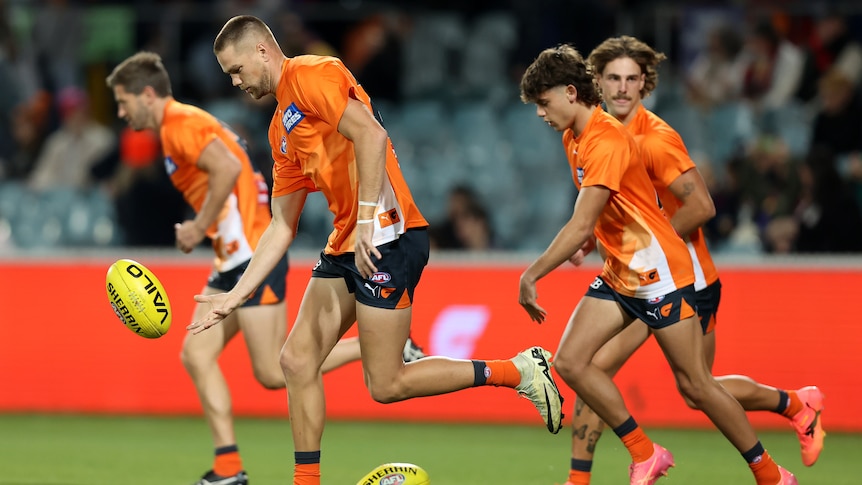 A group of GWS players run and bounce the ball in a warm-up drill ahead of a match.