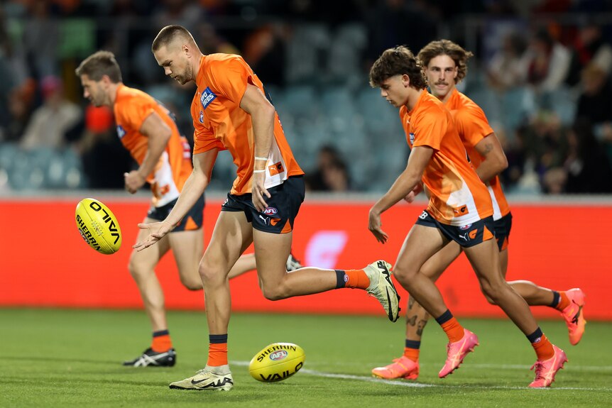A group of GWS players run and bounce the ball in a warm-up drill ahead of a match.