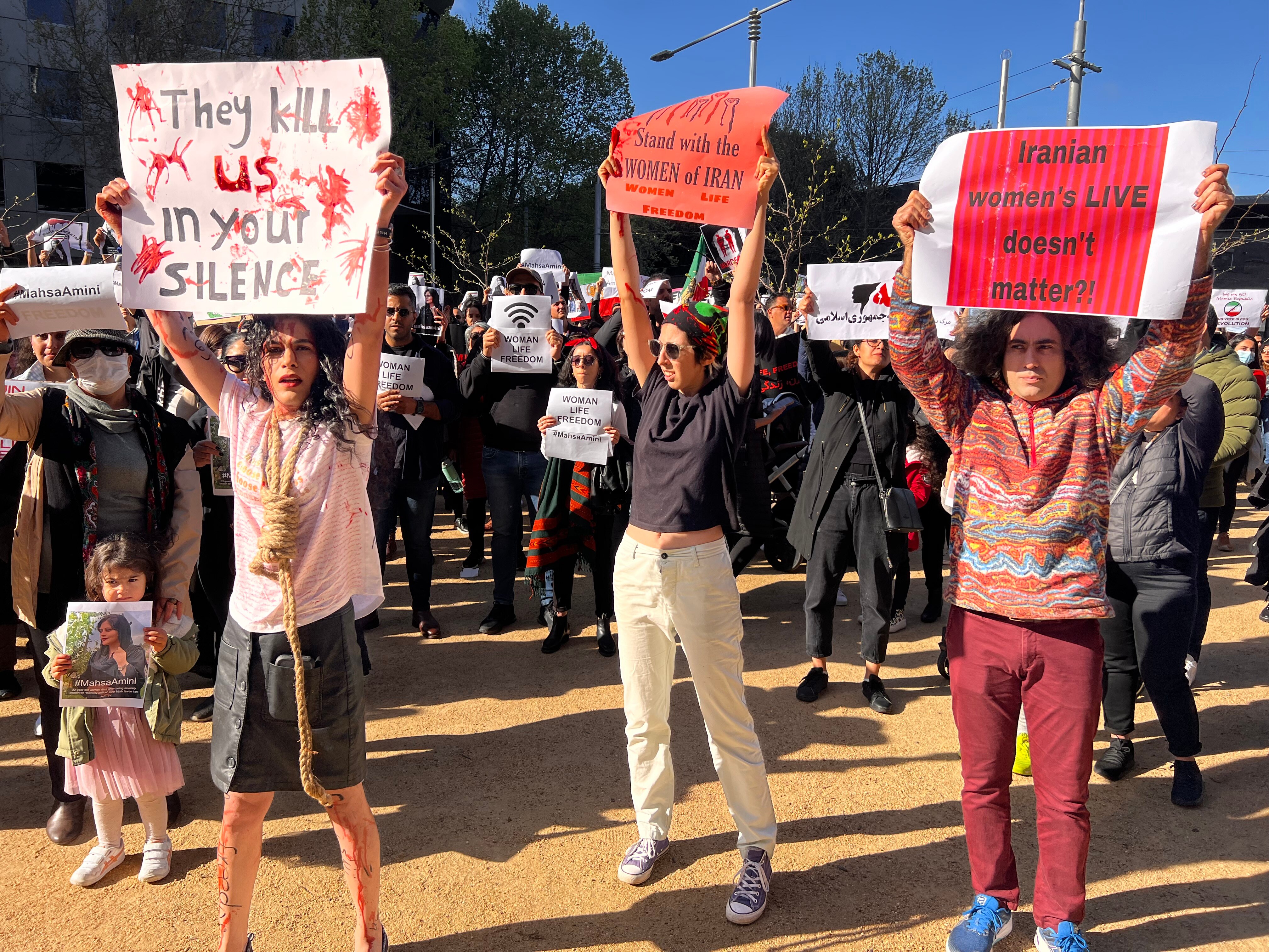Protesters gather, holding placards reading 'They kill us in your silence' and other messages in support of women's rights.