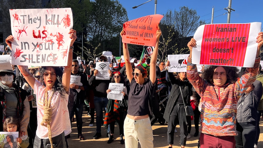 Protesters gather, holding placards reading 'They kill us in your silence' and other messages in support of women's rights.