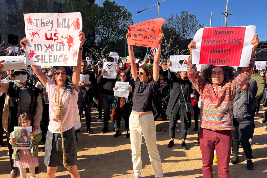 Protesters gather, holding placards reading 'They kill us in your silence' and other messages in support of women's rights.