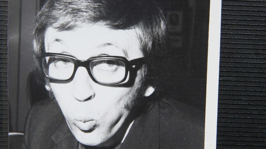 A young man with thick black glasses pulls a funny face.