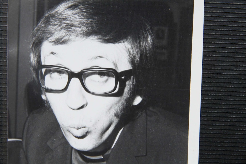 A young man with thick black glasses pulls a funny face.