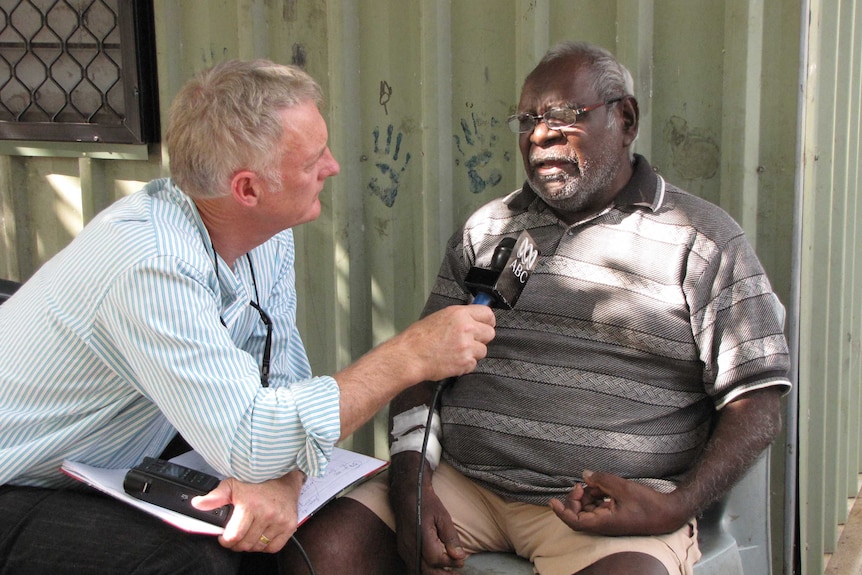 Tony Eastley holds a microphone while interviewing a Darwin man in 2010.