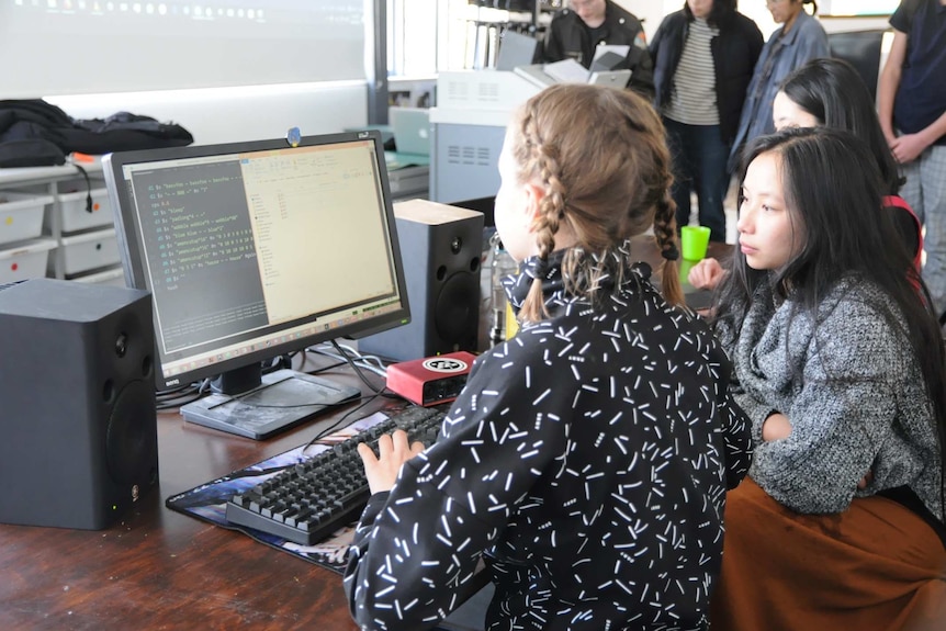 two people looking at a desktop computer, while one types