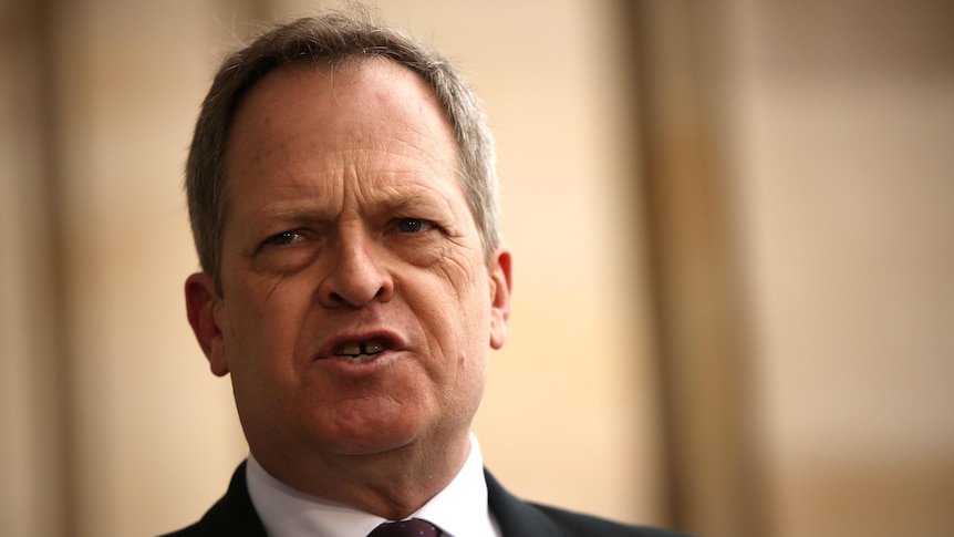 A man in a black suit speaks at a press conference