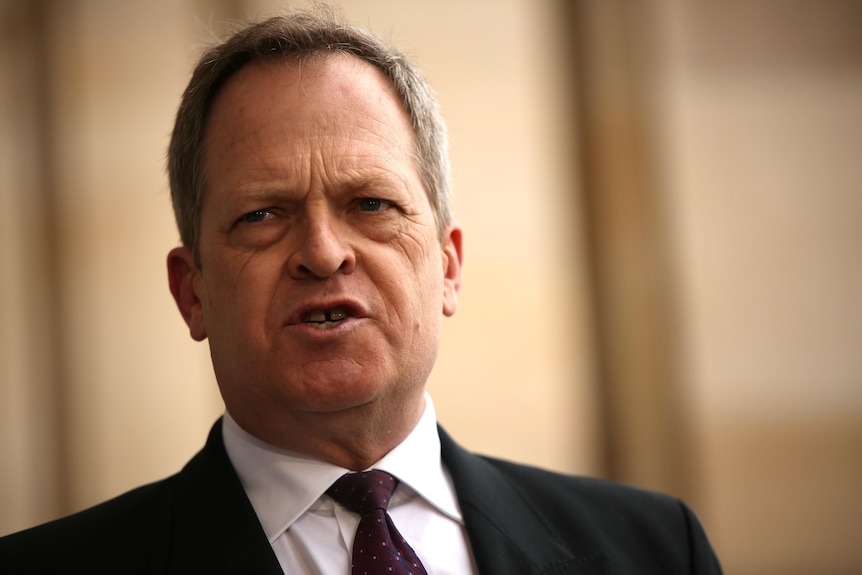 A man in a black suit speaks at a press conference