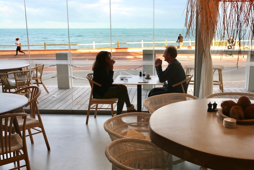 A man and woman sit at a table in The Little Bay in Watermans, outside people run along the footpath