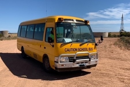 A bright yellow school bus parked in red sand.