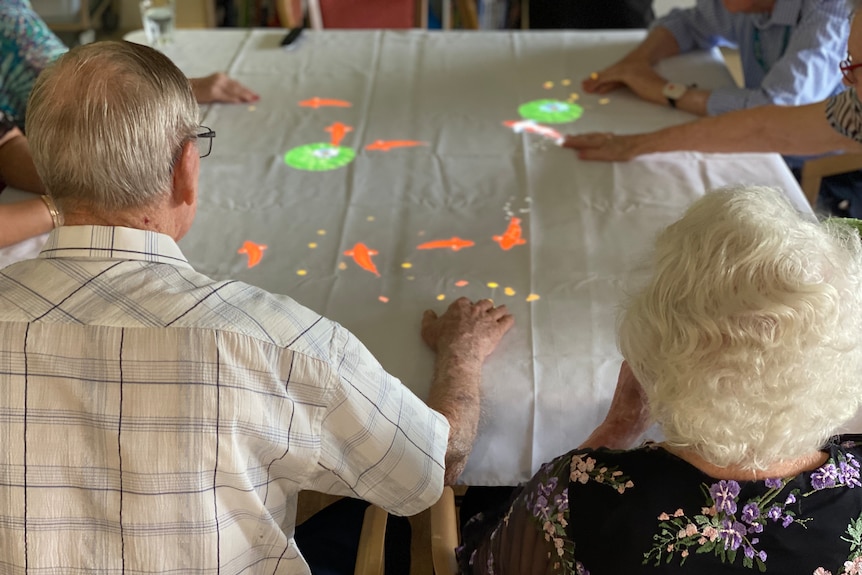 Aged care residents sit around a table that has flouro lights on it